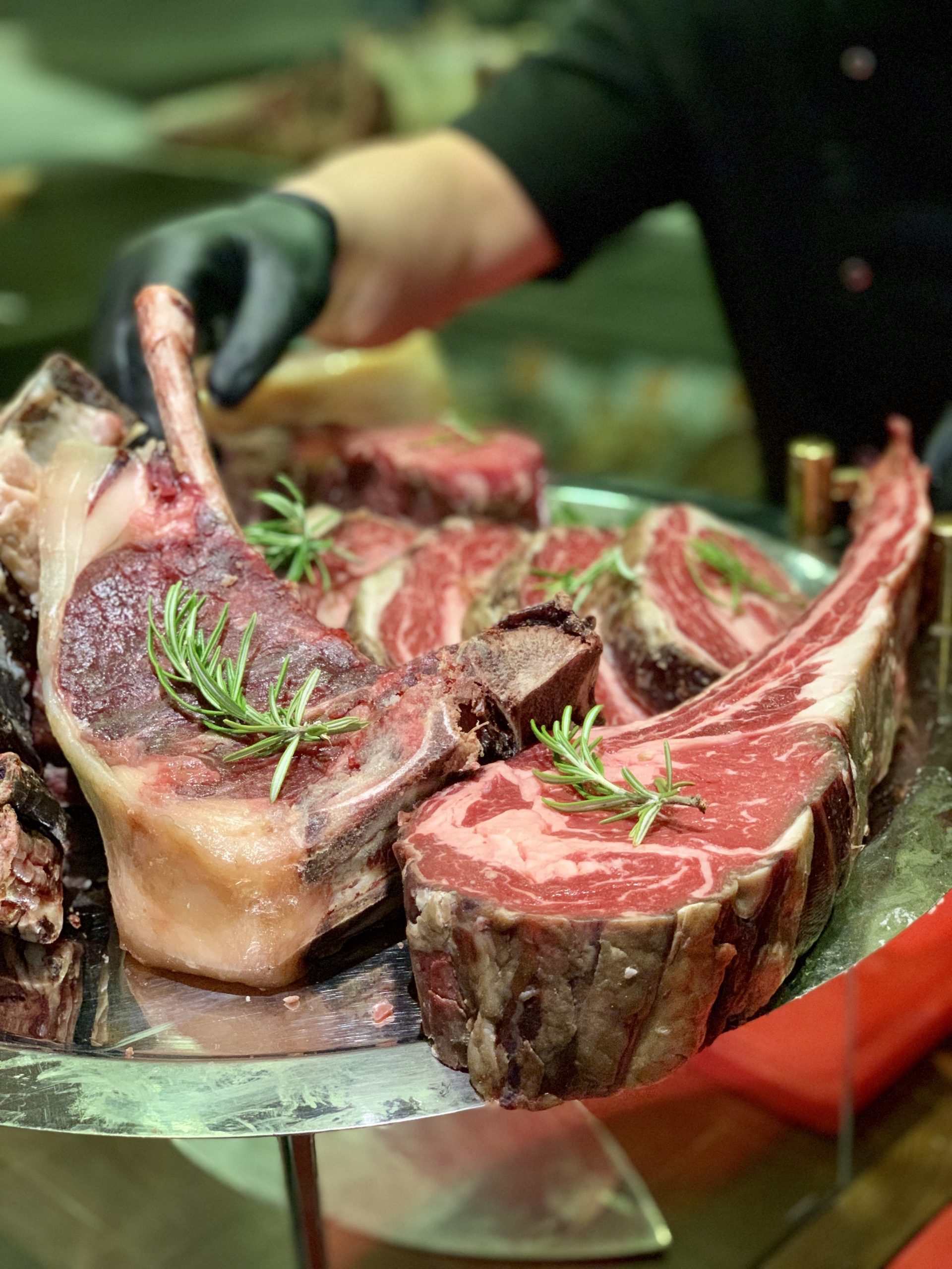 A closeup of cooked red meat on a metal plate with the chef in the background